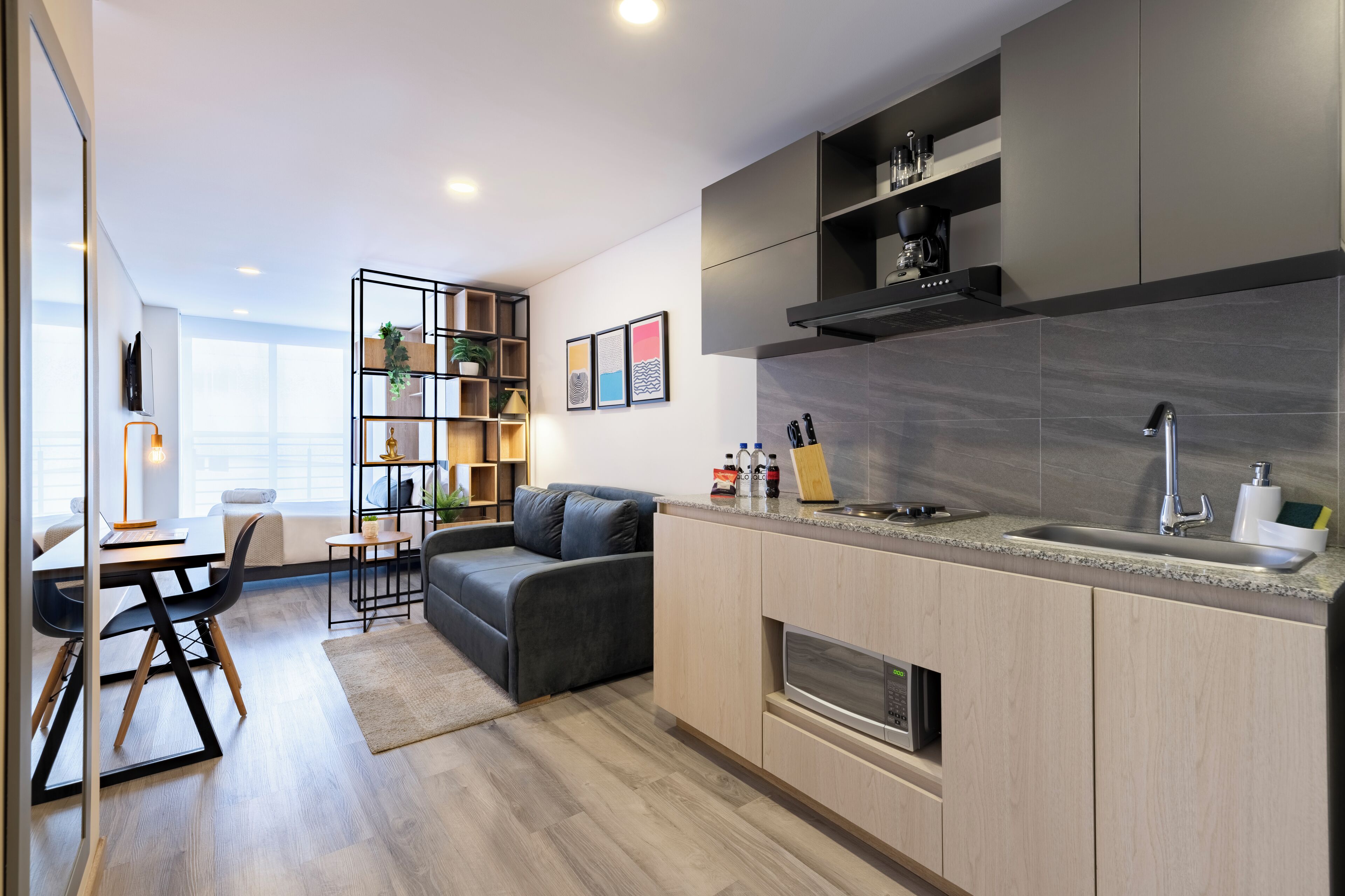 A modern kitchen with a built-in oven, a sink, and a countertop. There is a dining area with a table and chairs, and a sofa.