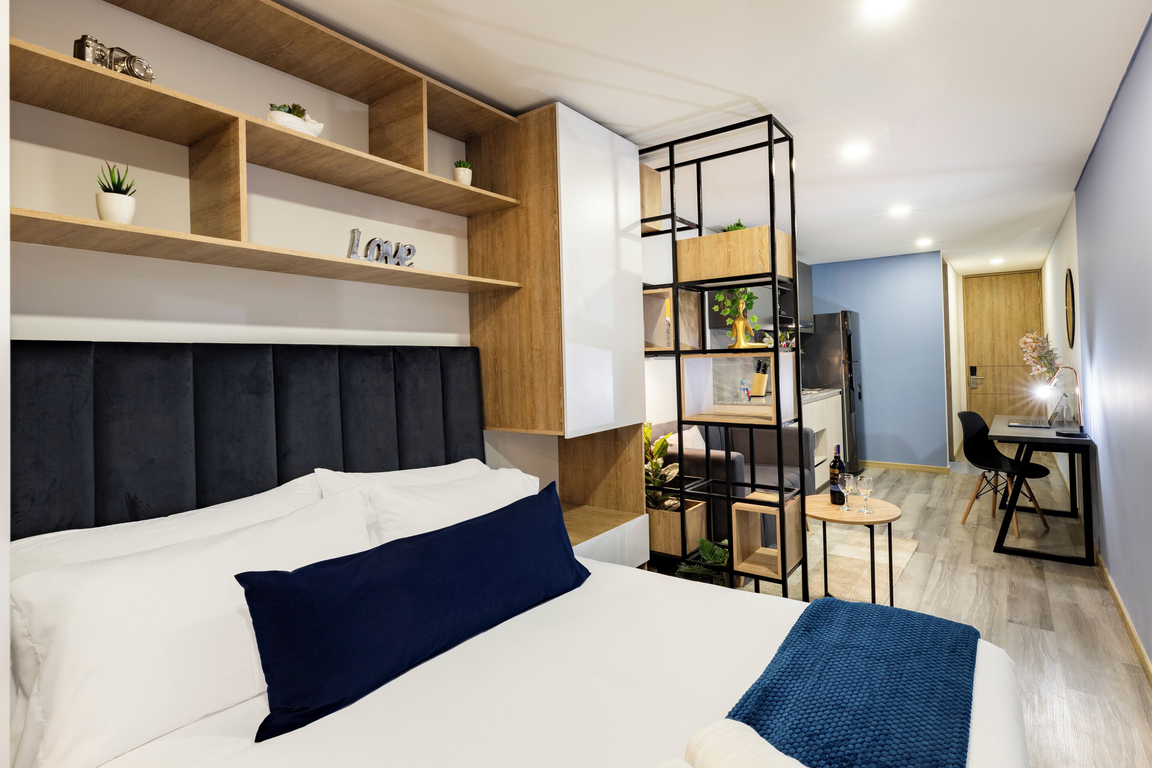 Una habitación de hotel moderna con una cama grande, un escritorio y estanterías empotradas con plantas.