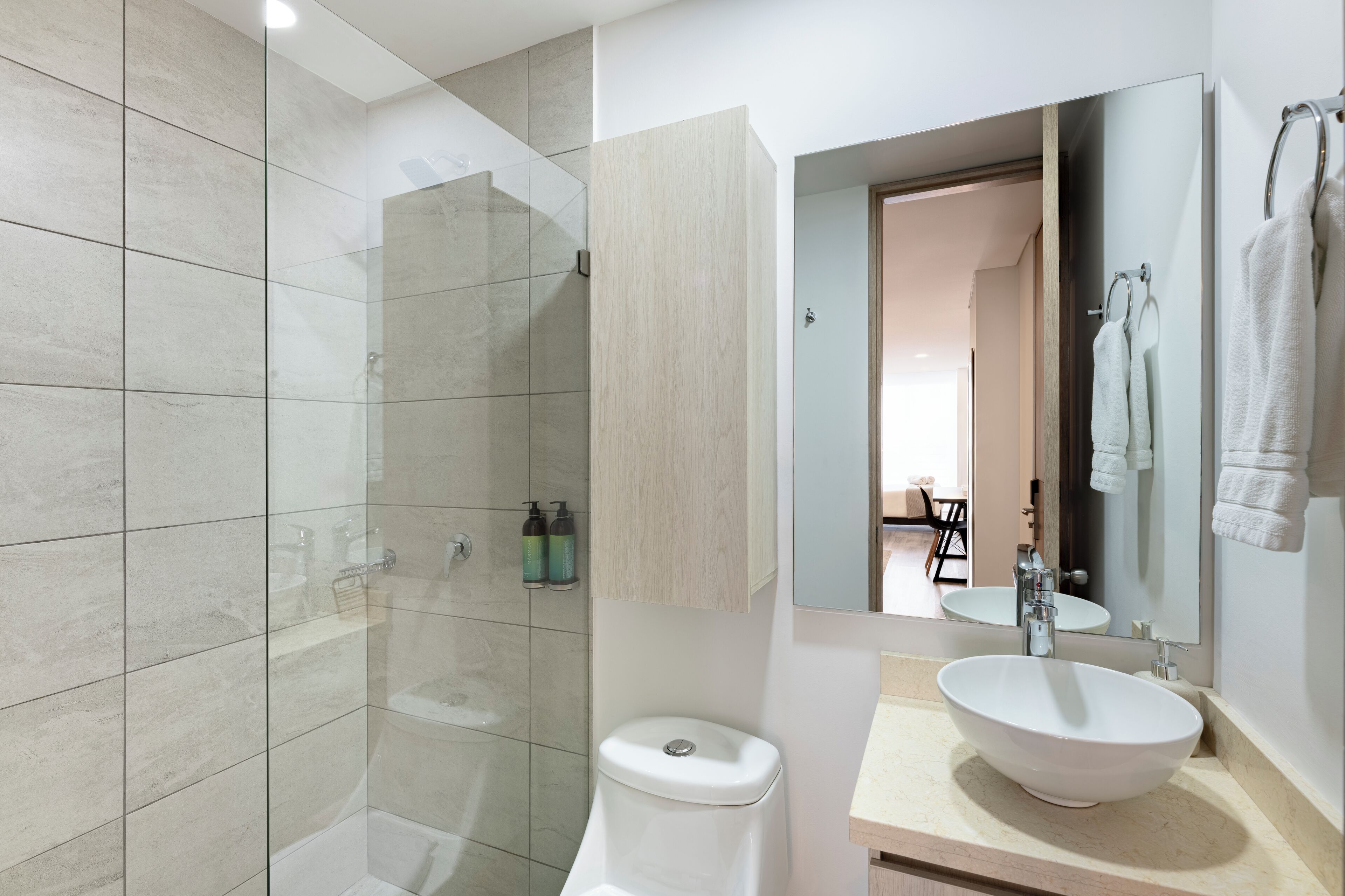 Ein modernes Badezimmer mit einer Duschkabine aus Glas, einer weißen Toilette, einem großen Waschbecken mit Spiegel darüber und einem Handtuchhalter.