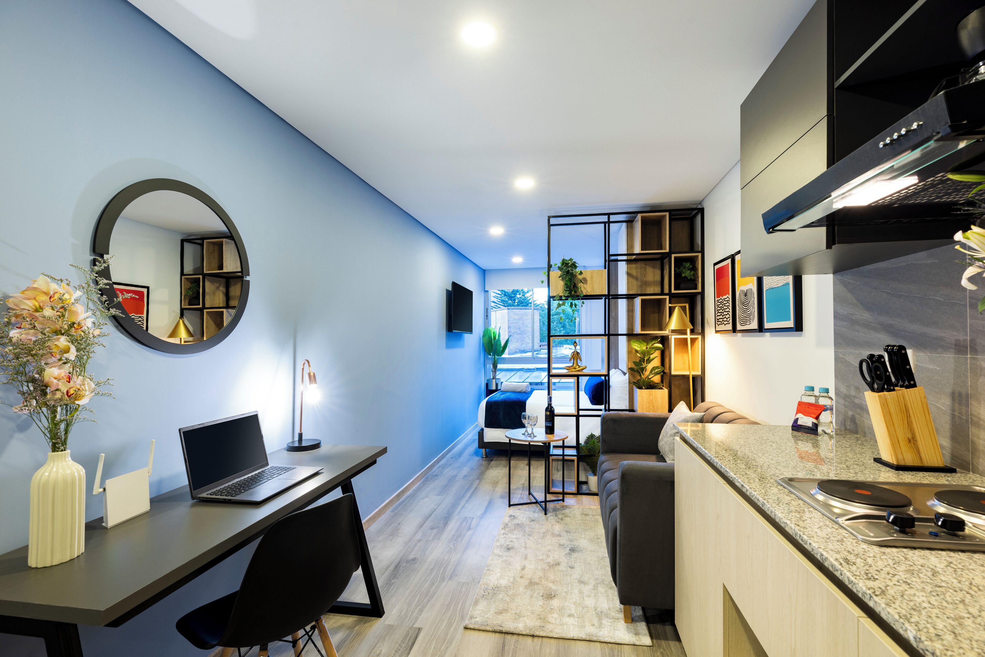 A modern kitchen with a built-in stove, a dining area with a laptop, and a living space with a sofa and a TV.