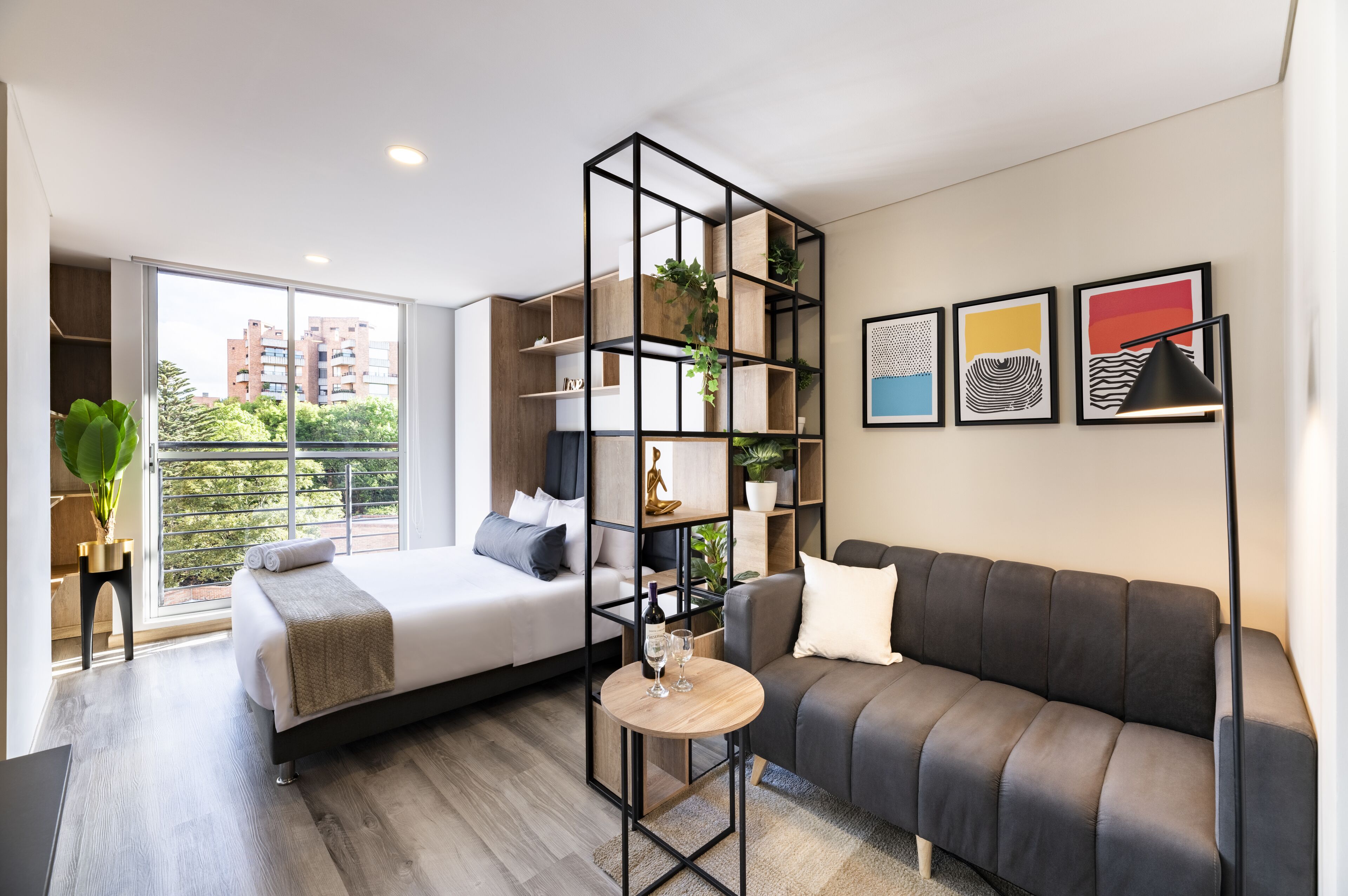 A modern bedroom with a bed, a sofa, a small table with glasses, and a plant.
