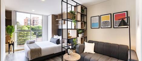 A modern bedroom with a bed, a sofa, a small table with glasses, and a plant.