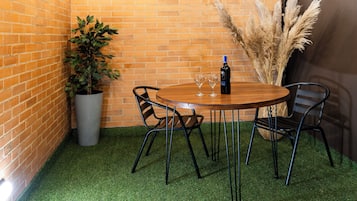 A corner room with a brick wall, a wooden table with chairs, a potted plant, and pampas grass.