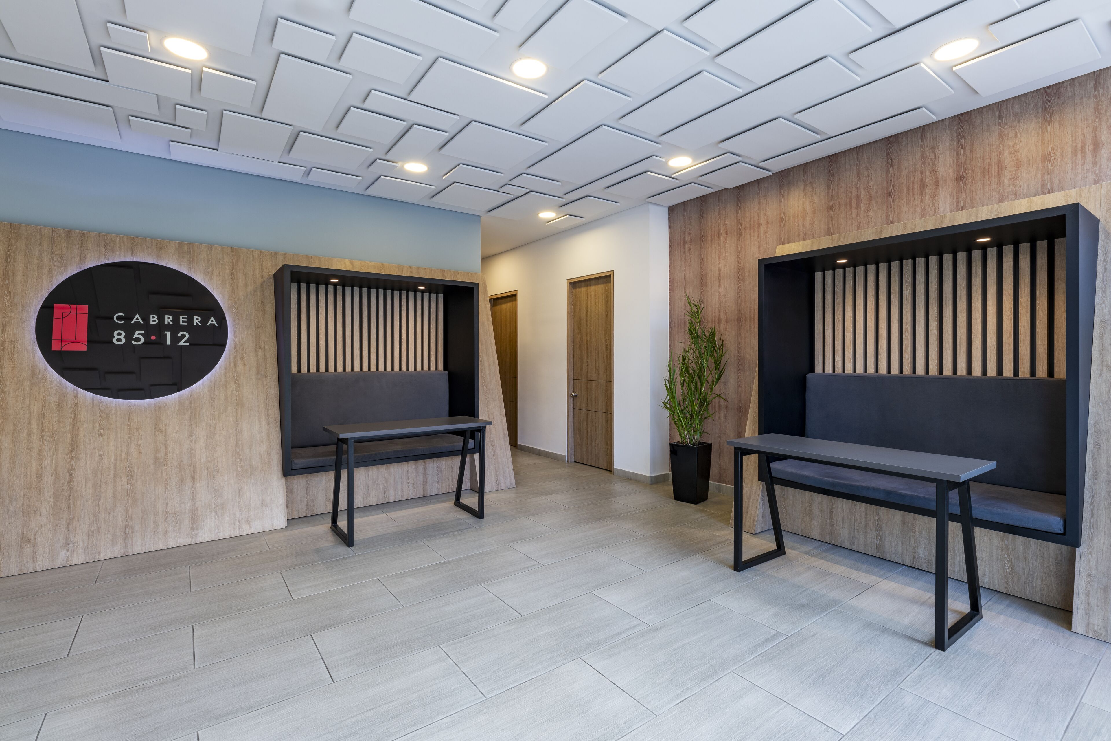 A modern reception area with a wooden wall, a circular sign indicating room number 85-12, and two black benches.