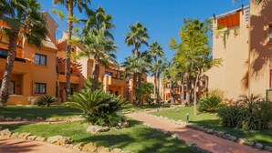 Ein Innenhof eines Resorts mit Palmen, einem gepflasterten Weg und mehrstöckigen Gebäuden mit Balkonen.