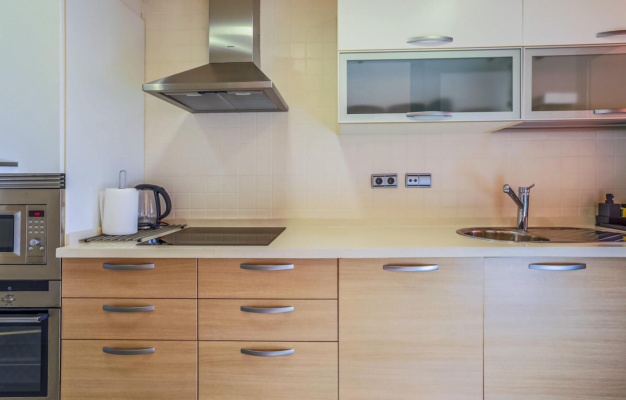 Une cuisine moderne dotée d’appareils électroménagers en acier inoxydable, de meubles en bois et d’un four à micro-ondes encastré.