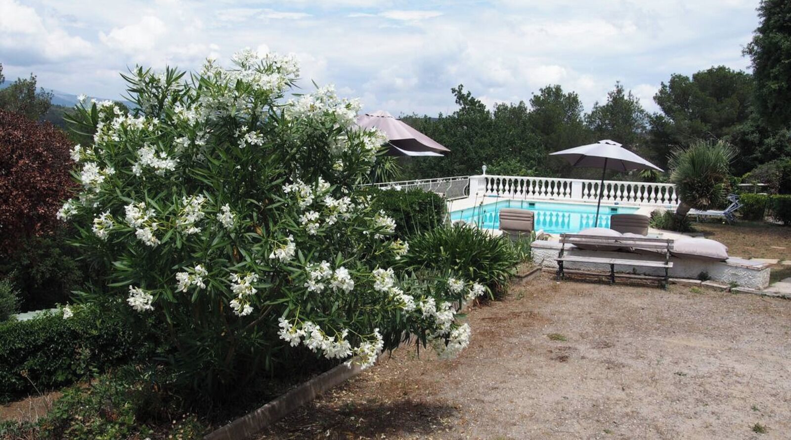 Ein Poolbereich mit weißem Zaun, Liegestühlen und einer Pergola mit Sonnenschirmen.