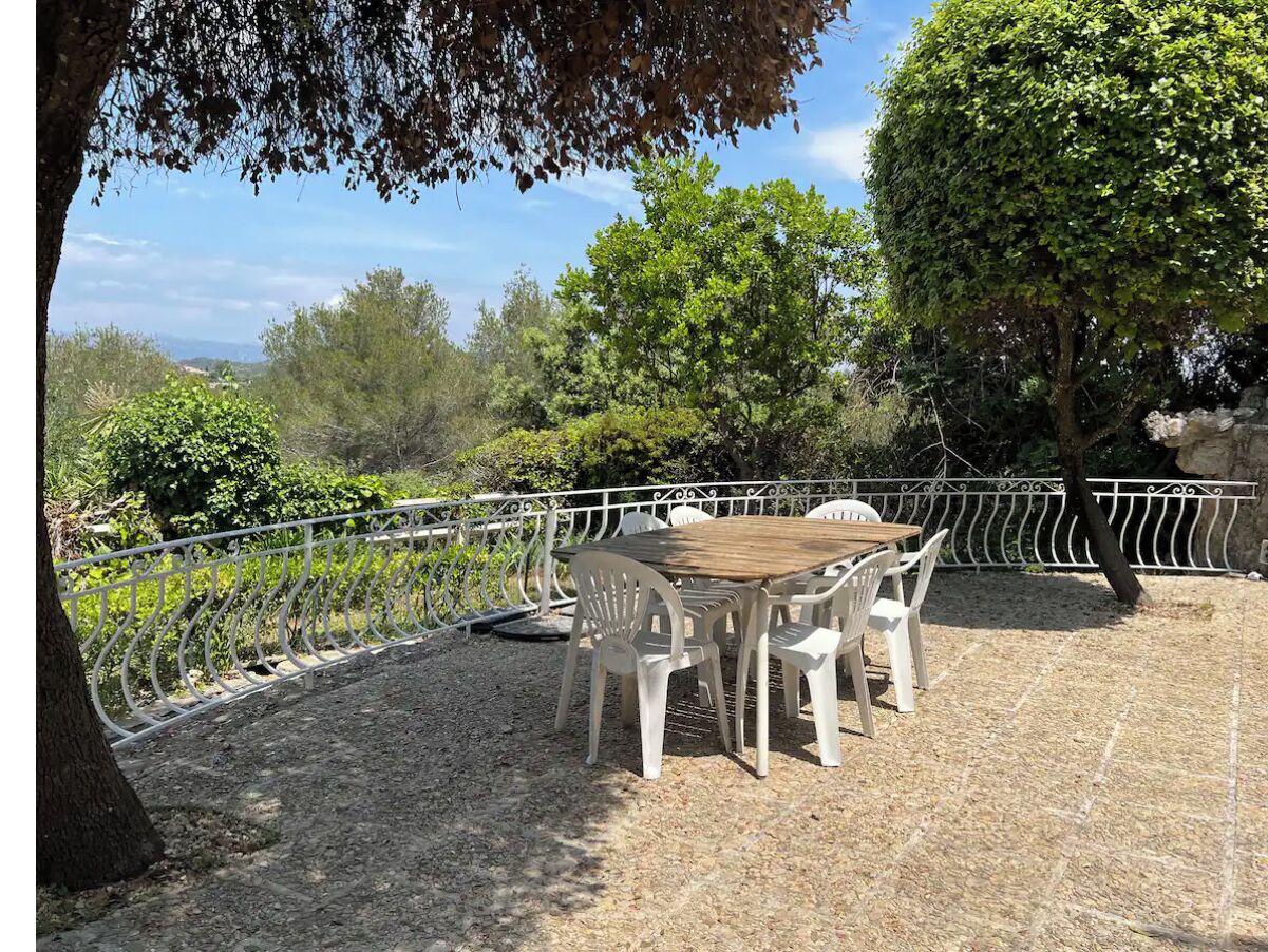 Une terrasse extérieure avec une table ronde et des chaises en plastique blanc, entourée d’une clôture en métal blanc.