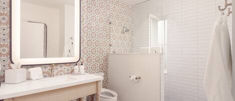 Een badkamer met een grote spiegel, een wastafel met toiletartikelen, een toilet en een douche.
