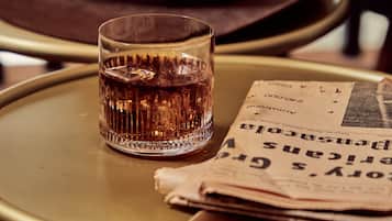 A glass of whiskey on a small round table with a newspaper and a brown hat.