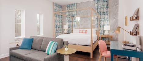A bedroom with a four-poster bed, a gray sofa, a small round table, a desk, and a chair.