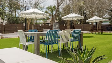 Un patio al aire libre con una mesa y sillas de madera, rodeado de sombrillas blancas y una valla de madera.