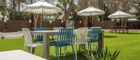 Un patio al aire libre con una mesa y sillas de madera, rodeado de sombrillas blancas y una valla de madera.
