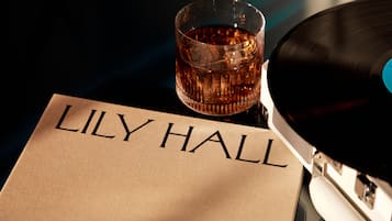 A vinyl record, a glass of amber liquid, and a beige fabric with "LILY HALL" printed on it.
