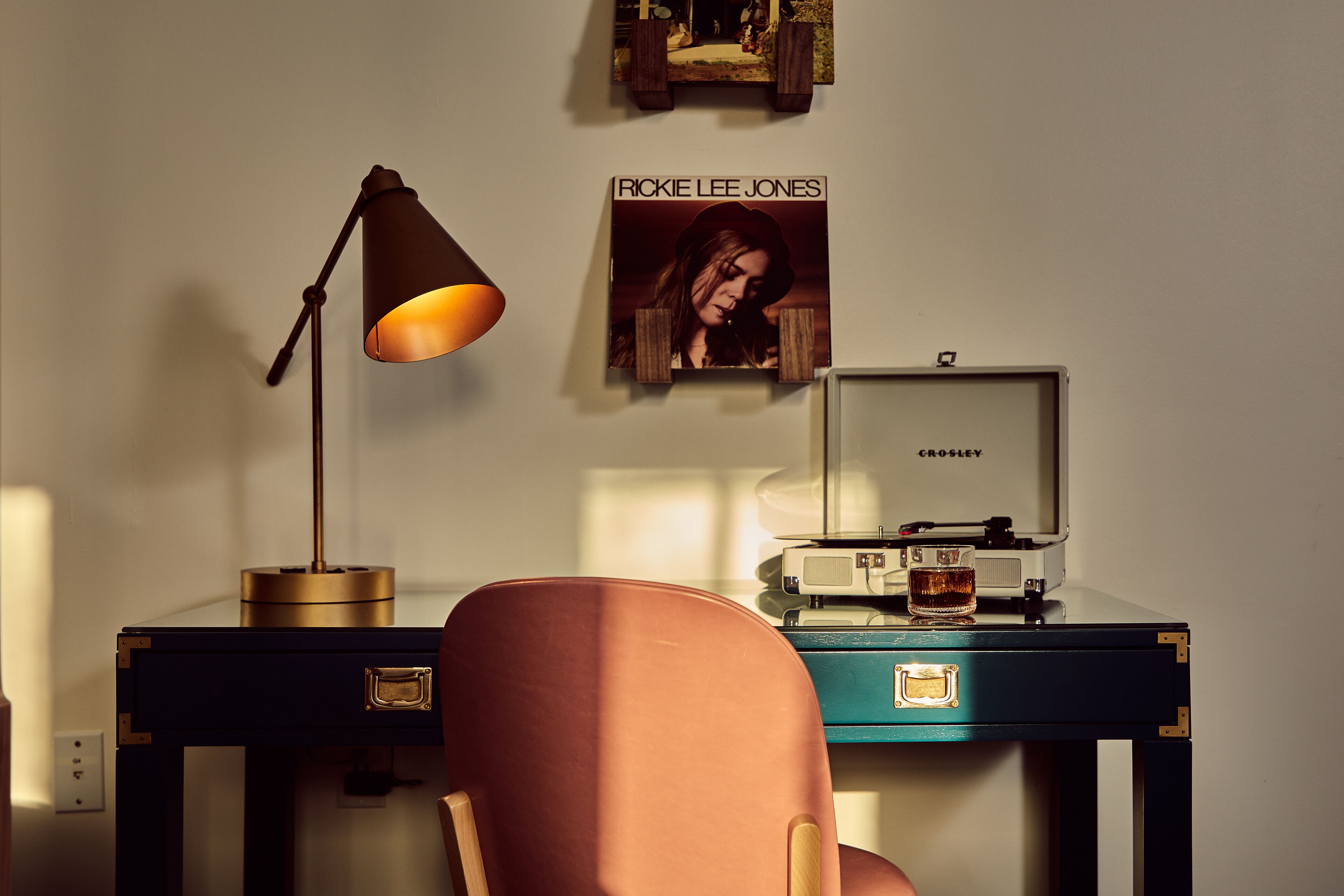 A desk with a lamp, a vintage record player, and a poster on the wall.