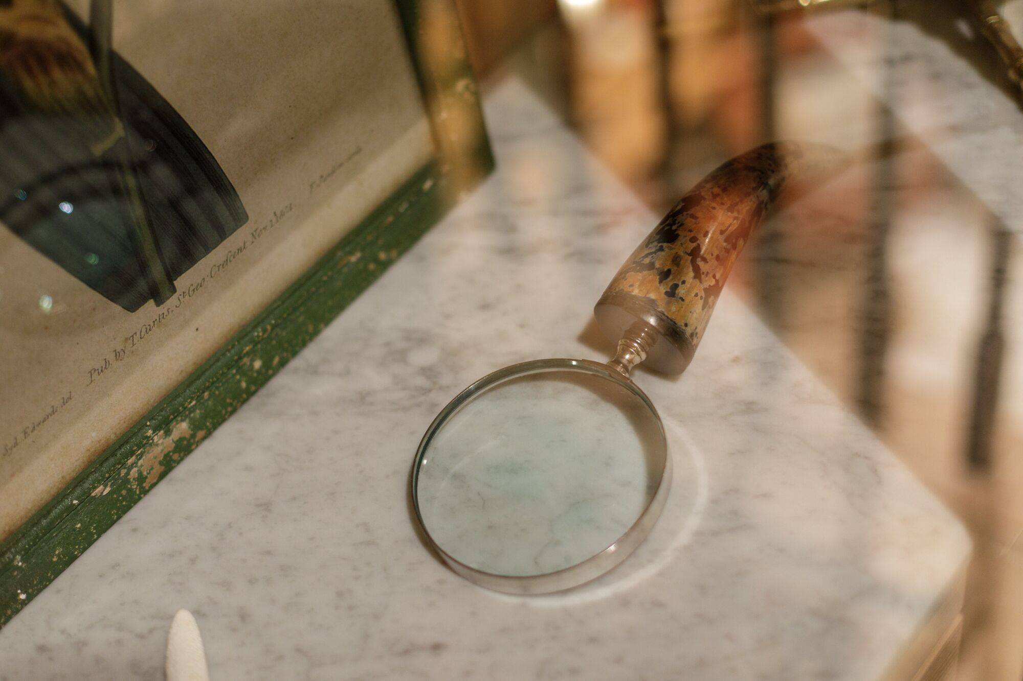 Una lupa sobre una superficie de mármol con un libro desgastado y un objeto de madera cerca.