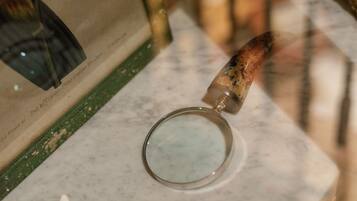 Una lupa sobre una superficie de mármol con un libro desgastado y un objeto de madera cerca.