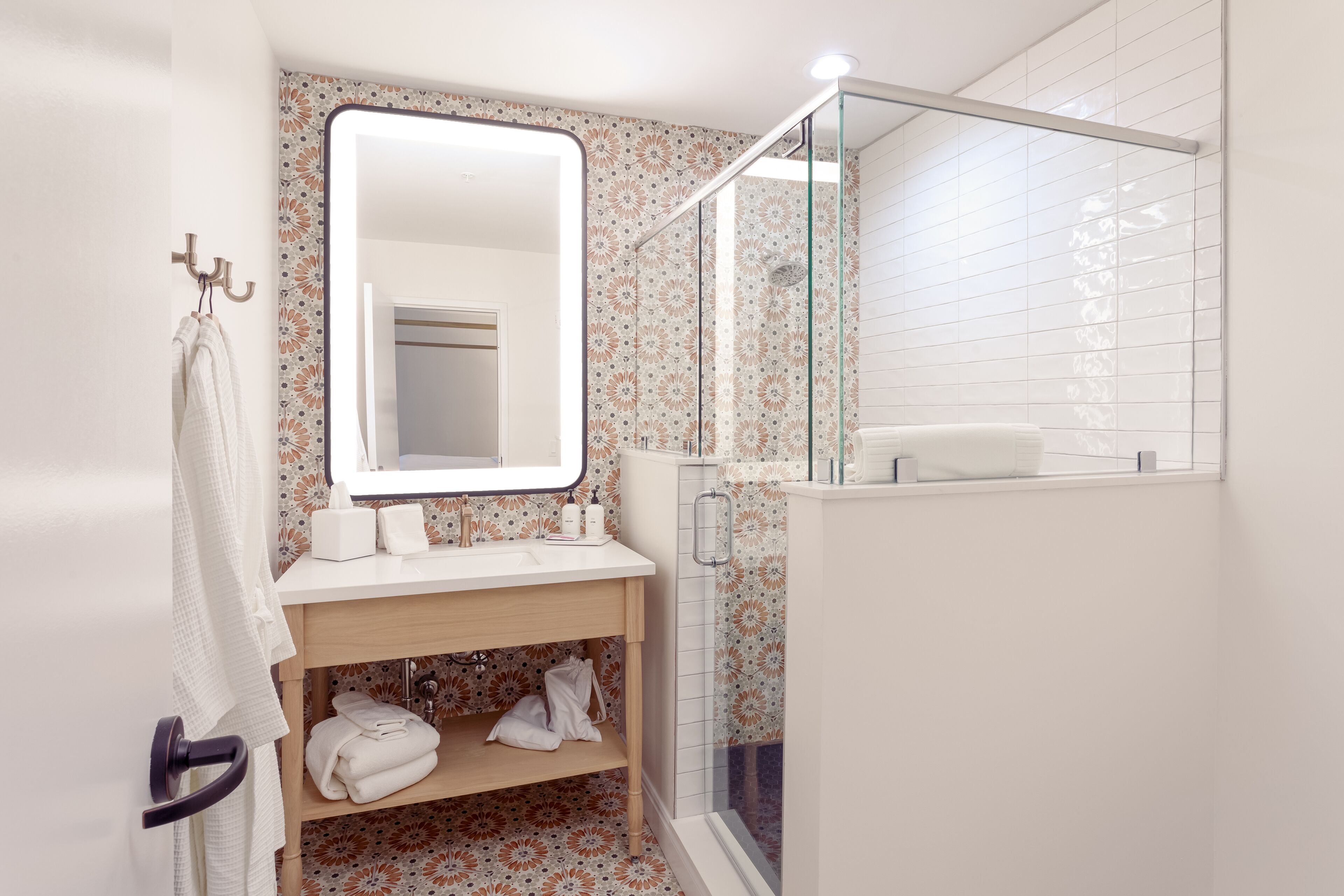 Une salle de bain avec un lavabo blanc, un miroir et une douche. On y trouve des serviettes et des articles de toilette sur le lavabo.