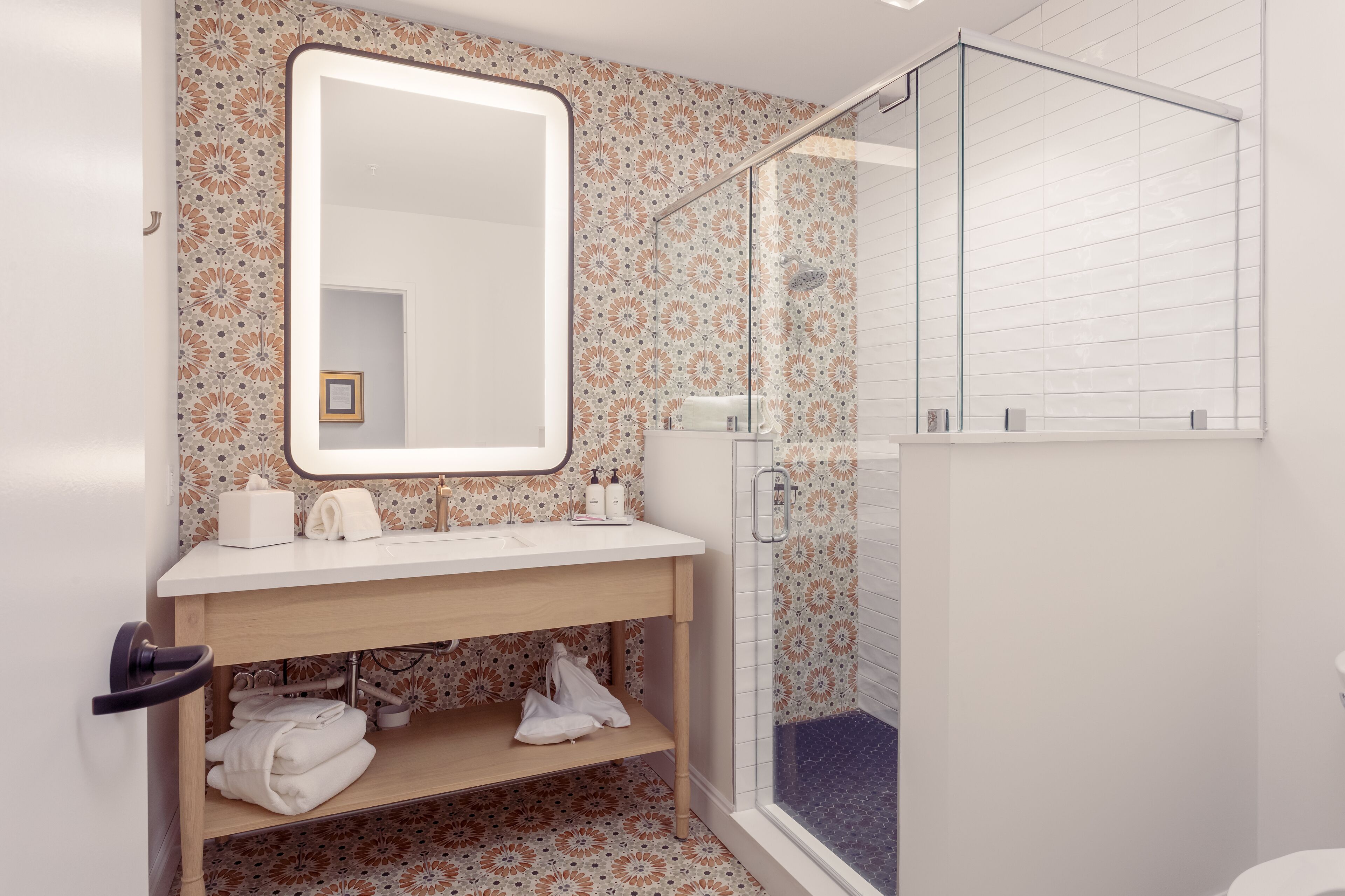 A bathroom with a wooden vanity, a large mirror, a shower with a glass door, and patterned tiles.