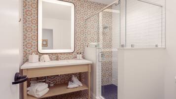 A bathroom with a wooden vanity, a large mirror, a shower with a glass door, and patterned tiles.