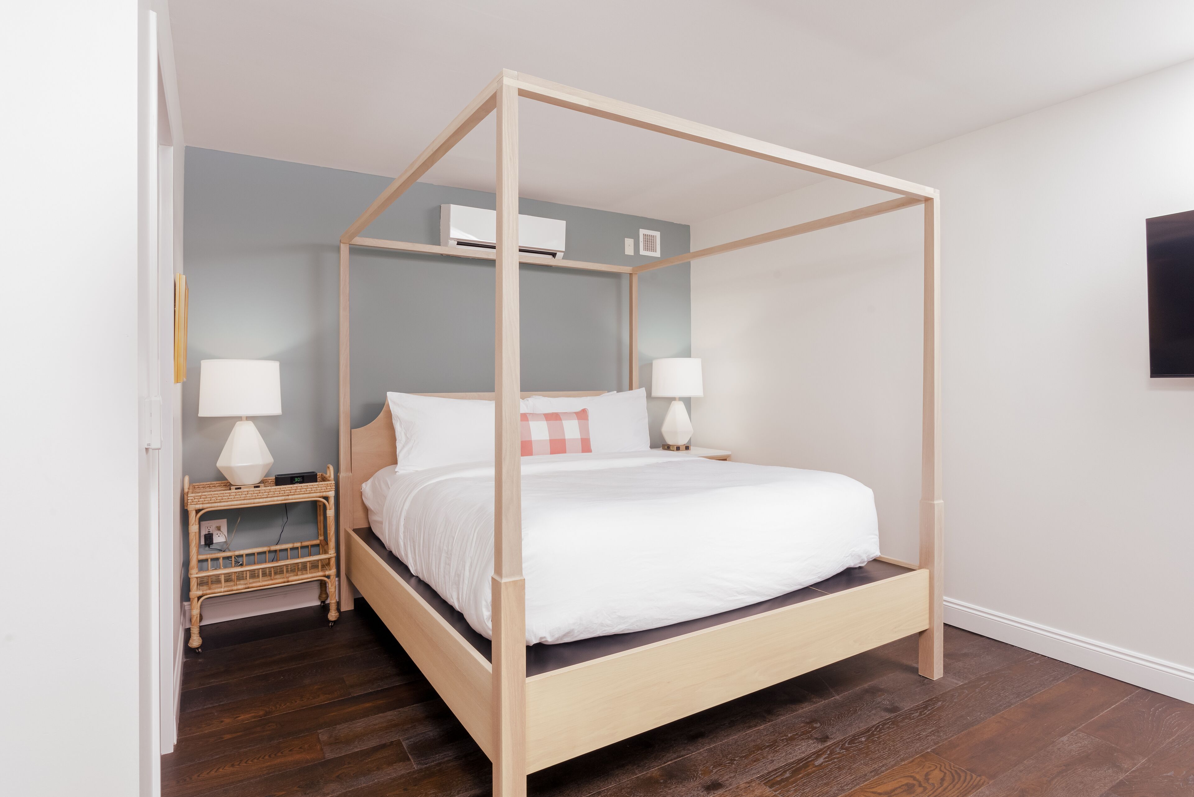 Una cama con dosel de madera, ropa de cama blanca y dos mesitas de noche con lámparas.