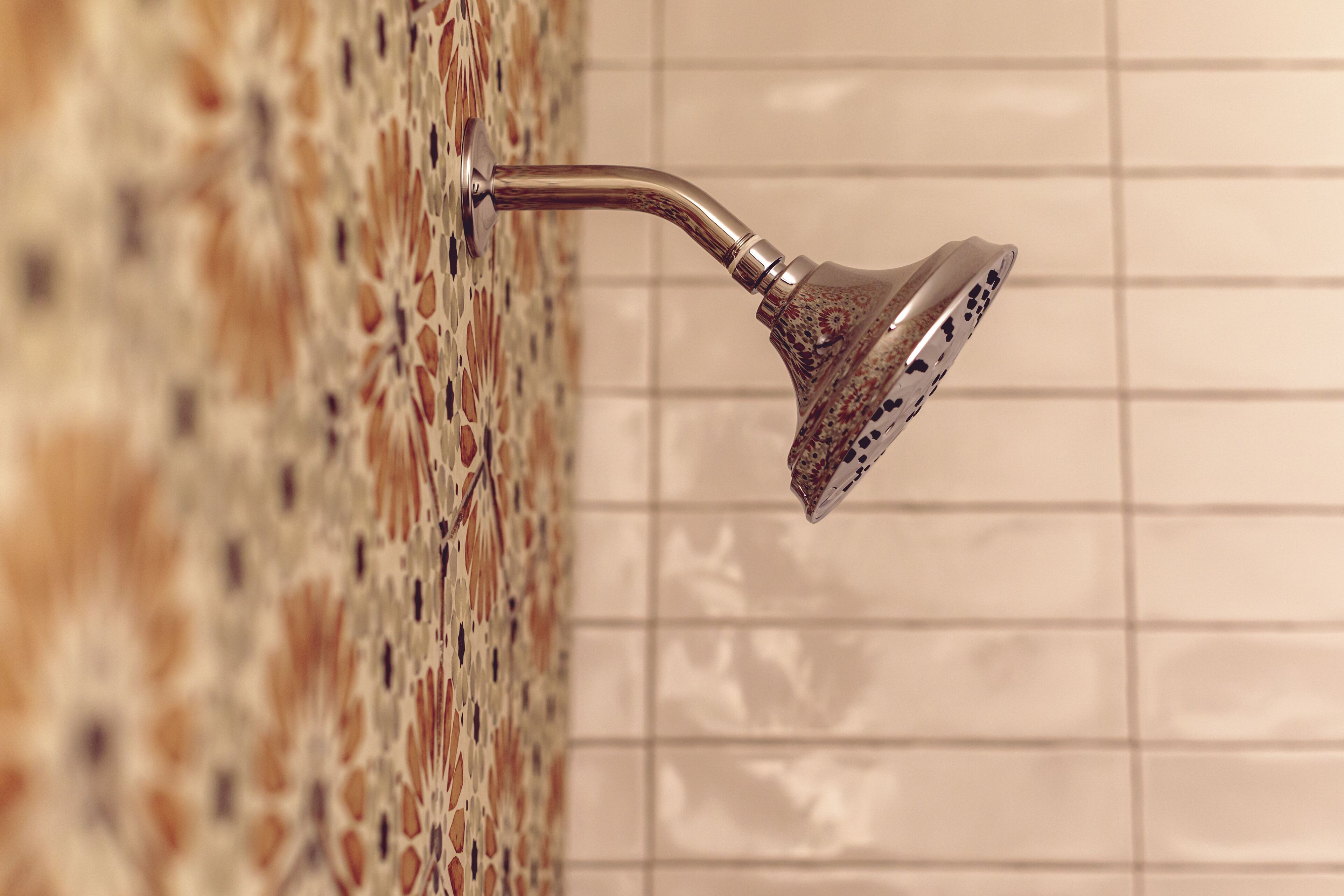 Un pommeau de douche fixé à un mur recouvert de carreaux formant un motif décoratif.
