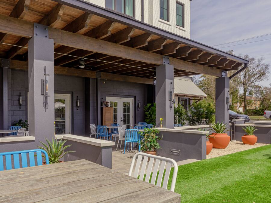 An outdoor patio area with wooden tables and blue chairs, a covered seating area, and potted plants.
