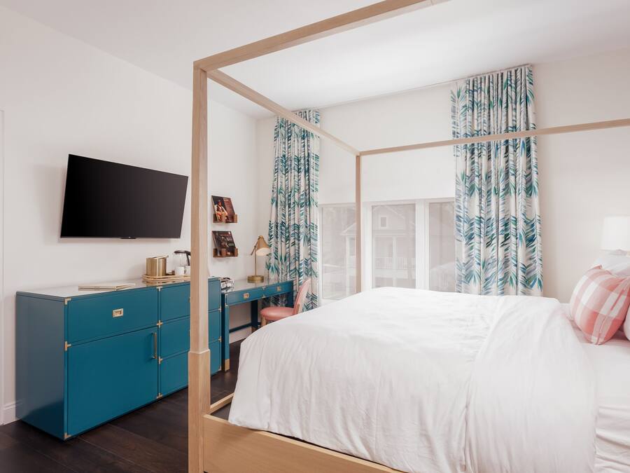 Un dormitorio con cama con dosel, un escritorio con silla, un televisor montado en la pared y un armario.