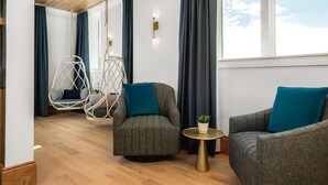 A modern room with a wooden ceiling, a hanging chair, two armchairs, a small round table, and a view of the sky through a large window. - Lily Hall- A Boutique Hotel (Pensacola)