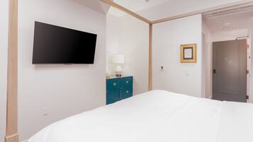 A hotel room with a bed, a flat-screen TV mounted on the wall, a dresser, a lamp, and a door.