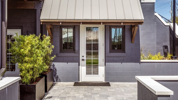 A modern building with a grey facade, a white door with glass panels, and a small porch area with a bench. - Lily Hall- A Boutique Hotel (Pensacola)