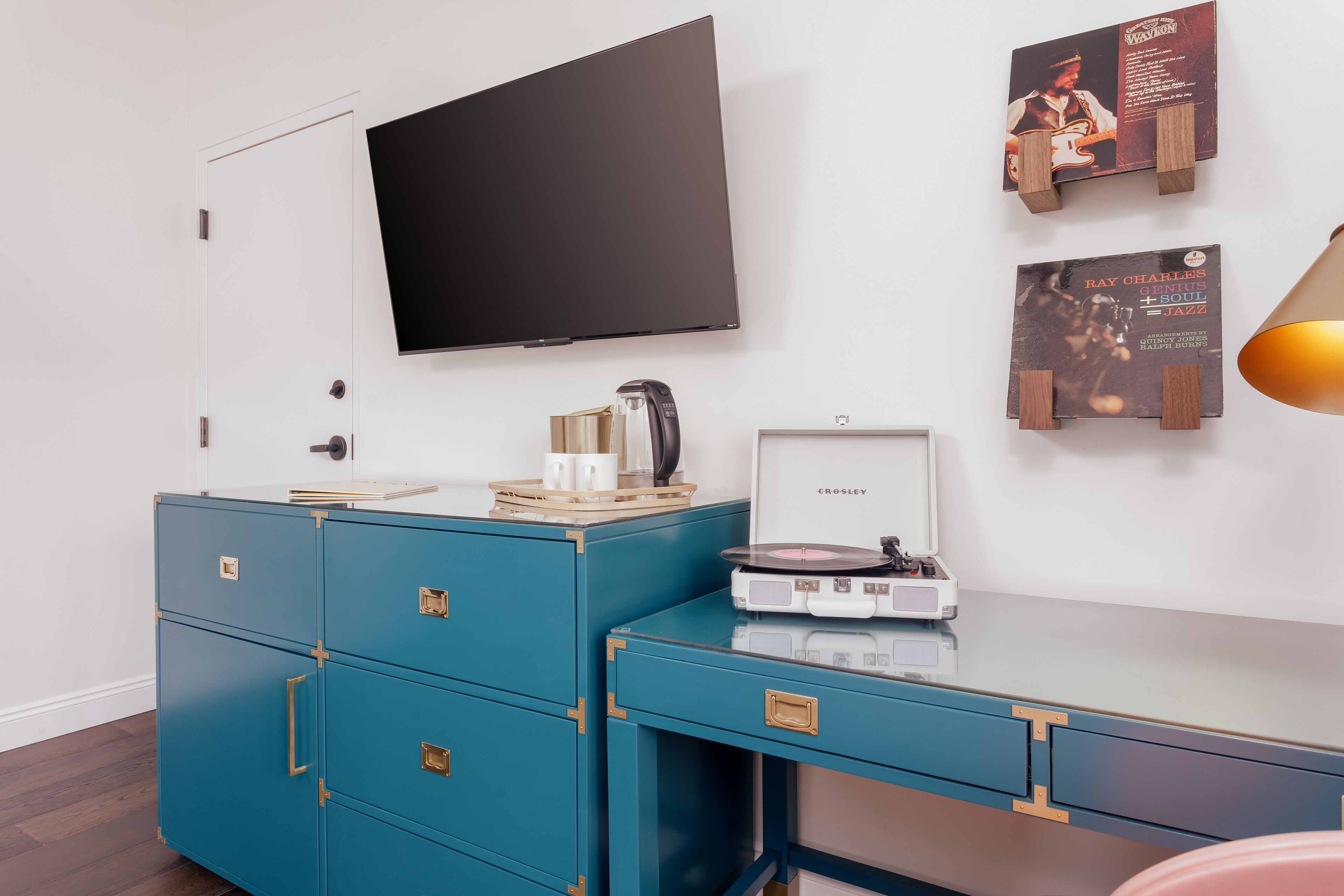 Una habitación moderna con un televisor de pantalla plana montado en la pared, un aparador azul con cajones, una mesita con un tocadiscos y dos carteles enmarcados en la pared.