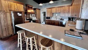 Une cuisine moderne avec des meubles en bois, un grand îlot central doté de tabourets, des appareils électroménagers en acier inoxydable et un éclairage encastré.