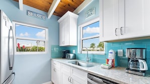 A kitchen with white cabinets, a stainless steel refrigerator, a coffee maker, and a view of the beach. - Beautiful Ground Floor 1bed/1.5 Bath Condo with Pool and Beach Access! (Siesta Key)