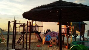 Ein Spielplatz mit einer Kletterkonstruktion, einer bunten Ballgrube und einem schattigen Bereich.