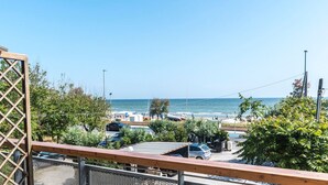 Blick auf die Küste vom Balkon mit Holzgeländer, mit Blick auf einen Strand, geparkte Autos und einen klaren Himmel.