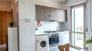 A compact kitchen with a washing machine, oven, and a window with a view.