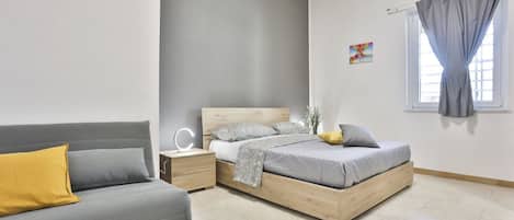 Un dormitorio con cama, sofá, mesita de noche y ventana con cortinas.