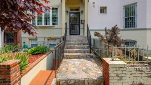 Eine Steintreppe führt zu einem Gebäudeeingang mit einem Ziegelpflanzkübel und einem Metallzaun.