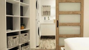 A hotel room with a wooden door, a white bed, a small bathroom with a mirror and sink, and a hallway with storage units. - Trocean View, Luxury Apartment with Amazing Ocean View (RIO GRANDE)