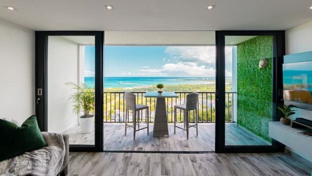 A balcony with a view of the ocean, a table with chairs, and a green wall. - Trocean View, Luxury Apartment with Amazing Ocean View (RIO GRANDE)