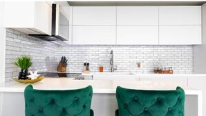 A modern kitchen with white cabinets, a white brick backsplash, and a central island with green upholstered chairs. - Trocean View, Luxury Apartment with Amazing Ocean View (RIO GRANDE)