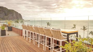 Enjoy the serene coastal views from this spacious outdoor space, featuring a long deck with comfortable seating and lush greenery.