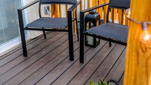 Eine Holzterrasse mit zwei schwarzen Stühlen und einem Korbwannenaufsatz mit Grünpflanzen.