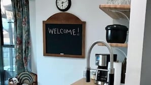 A kitchen with a wooden countertop, a sink, a blackboard with 'WELCOME!' written on it, a clock, and shelves with glassware and a black pot. - Cozy Family & Dog 4 Bedroom, 2 Bathroom Home (Harker Heights)
