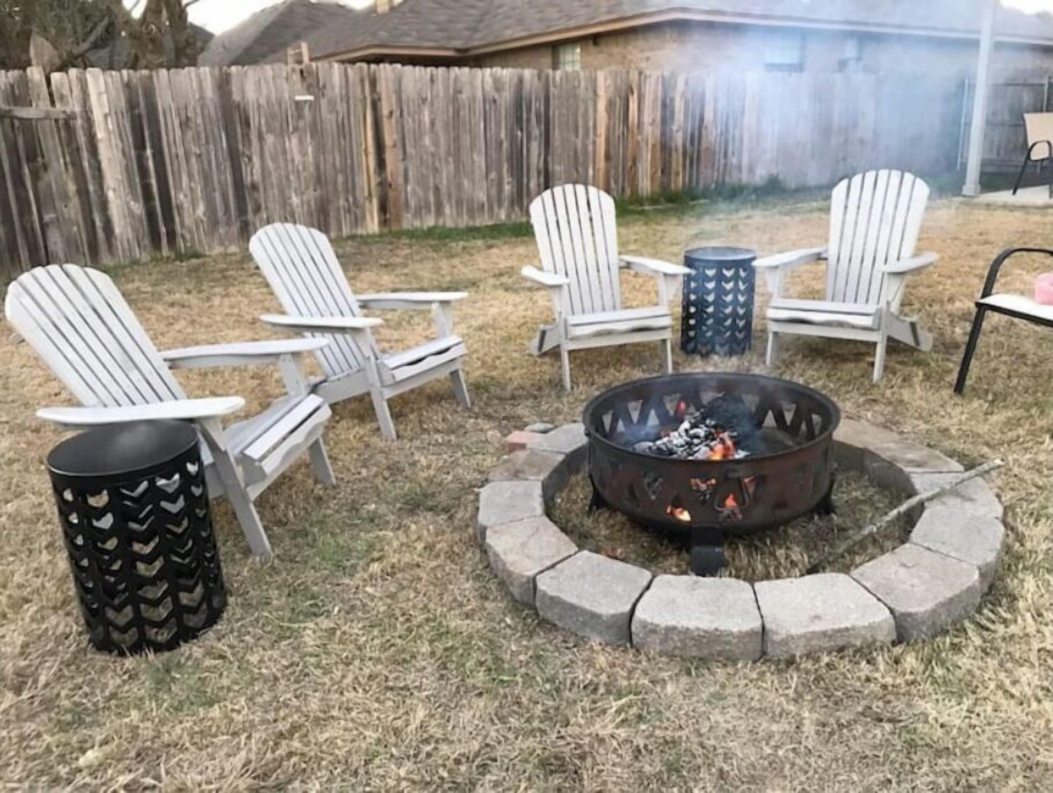 A backyard with a fire pit, four Adirondack chairs, and a metal trash can.