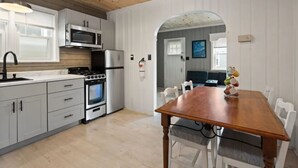 A kitchen with white cabinets, a wooden dining table, and a microwave. - 2 COTTAGES WITH A SHARED DECK 4 BEDROOMS, 2 BATHS, SLEEPS 8. VACATION TOGETHER (Seaside Heights)