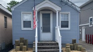 A blue single-story house with a white front door, two windows, and a small porch with steps. - 2 COTTAGES WITH A SHARED DECK 4 BEDROOMS, 2 BATHS, SLEEPS 8. VACATION TOGETHER (Seaside Heights)