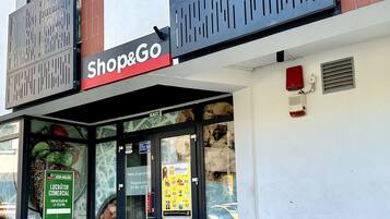 A Shop&Go store with a glass entrance, security signage, and a trash bin outside.