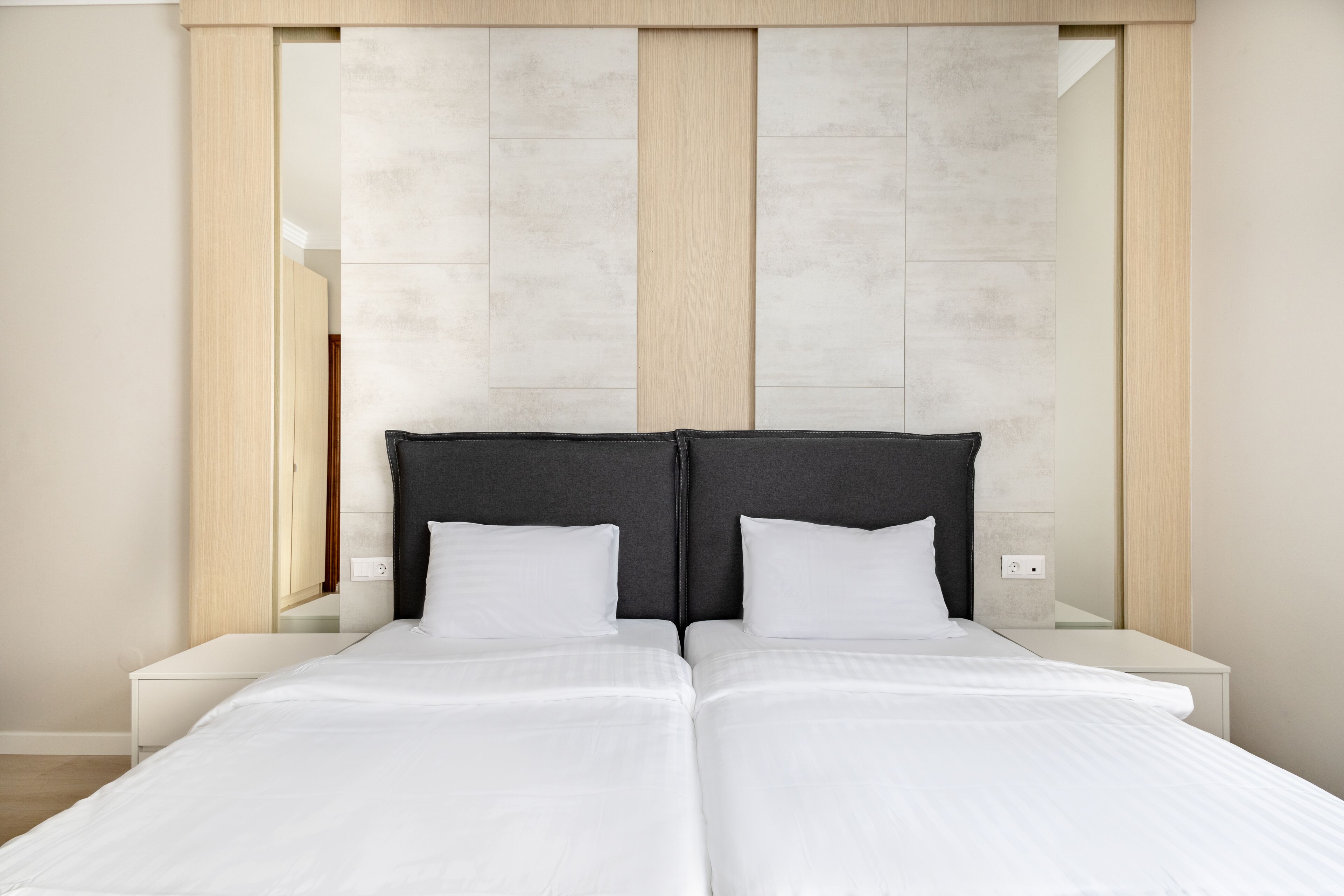 A modern bedroom with a large bed, a wooden headboard, and a white nightstand.